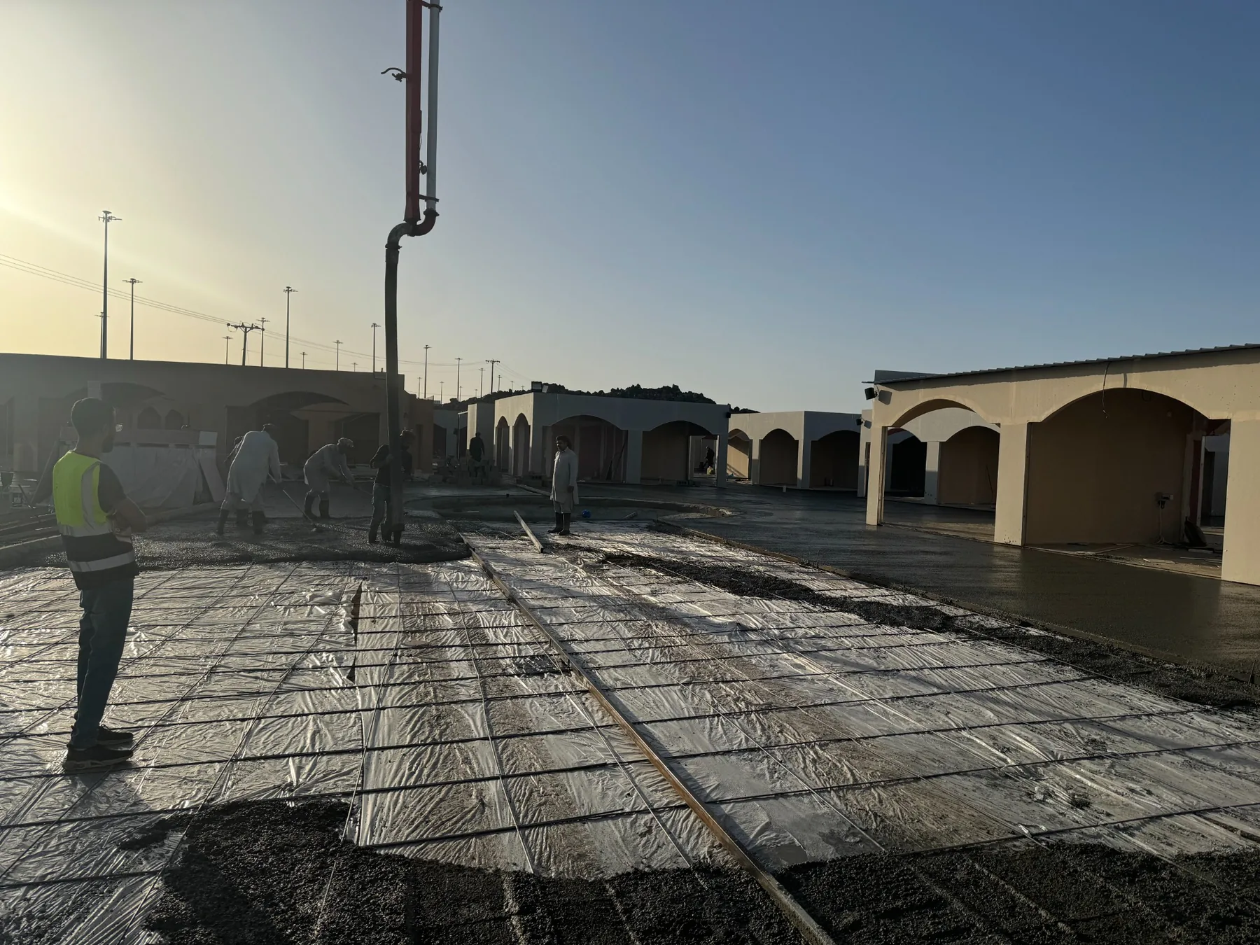 Construction workers developing the site beside arched structures at sunset.